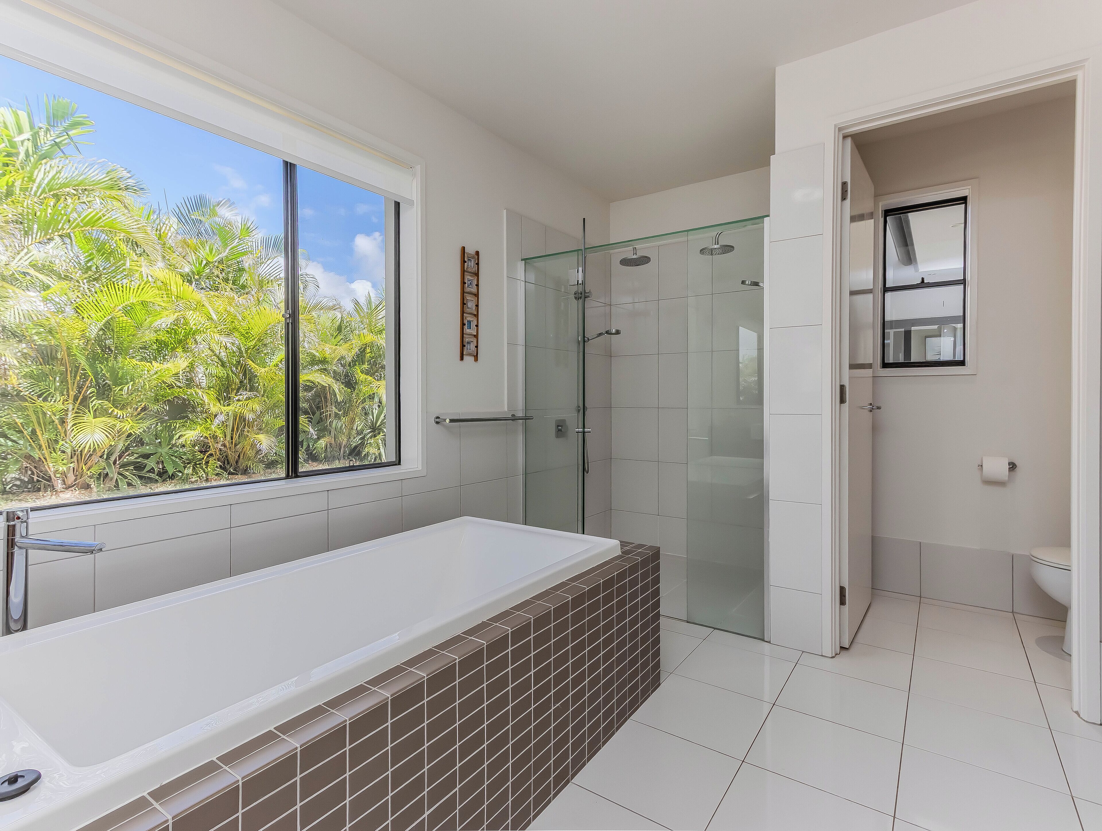 Ein modernes Badezimmer mit einer großen Badewanne, einer Duschkabine und einem Fenster mit Blick auf Grünflächen.