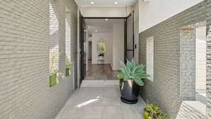 A narrow hallway with brick walls, potted plants, and a door leading to a room. - Longboard Coastal Retreat (Kingscliff)