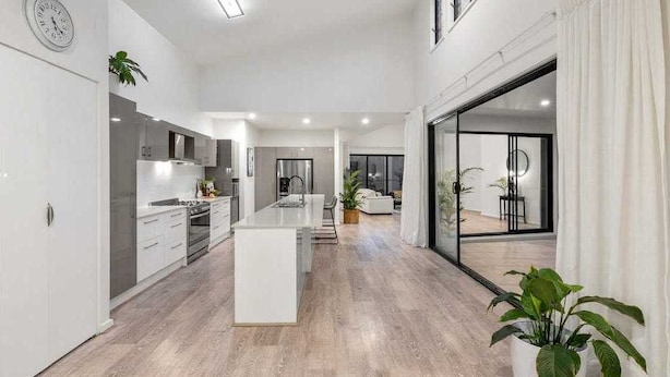 A modern kitchen with a central island, a dining area with a view, and a large sliding glass door leading to an outdoor space. - Longboard Coastal Retreat (Kingscliff)