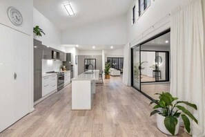 Et moderne køkken med en central ø, et spiseområde med udsigt og en stor skydedør til et udendørs område.