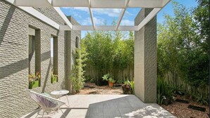 A covered patio with a brick wall, a white chair, and a small table. - Longboard Coastal Retreat (Kingscliff)