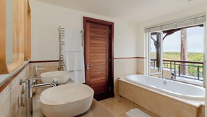 Une salle de bain dotée d’une grande baignoire, de deux lavabos, d’une porte en bois et offrant une vue sur l’extérieur.