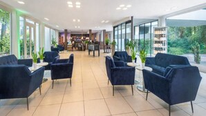 En rummelig lobby med mørkeblå siddepladser, et barområde og store vinduer med udsigt til grønne områder.