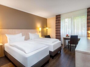 Habitación de hotel con dos camas, un escritorio, una silla y una lámpara.