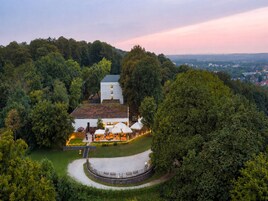 Un edificio grande rodeado de vegetación exuberante, con una zona de estar circular al aire libre y una escalera que conduce a la entrada.