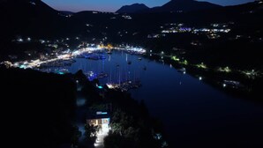 Vista nocturna d'una marina amb vaixells amarrats, envoltada de turons i edificis il·luminats.