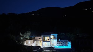 Una casa de dues plantes amb piscina, parets de pedra i vistes als turons circumdants.