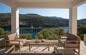 A balcony with a view of a lake and hills, furnished with two sofas and a table. - Villa Oliva – Seaside Charm with Village at Your Doorstep (Lefkada)