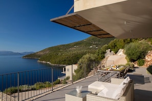 Ein Balkon mit Esstisch, Gartenmöbeln und Blick auf das Meer und die Hügel.