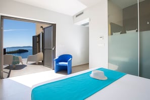 Ein modernes Hotelzimmer mit Balkon, einem blauen Sessel, einem weißen Bett und einem weißen Hut auf dem Bett.