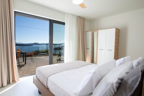 A bedroom with a bed, a wardrobe, a view of the outdoors, and a table with chairs. - Villa Katerina-Stylish 4DR villa with Sea View (Perigiali)