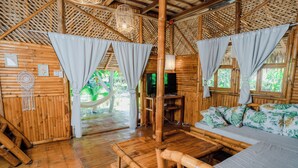 A bamboo-themed room with a bed, a TV, and a hammock. - Tongo Hill Cottages (Moalboal)