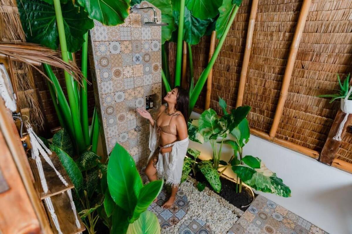 Un baño tropical con pared de ducha estampada, grandes plantas verdes y un fondo de bambú.