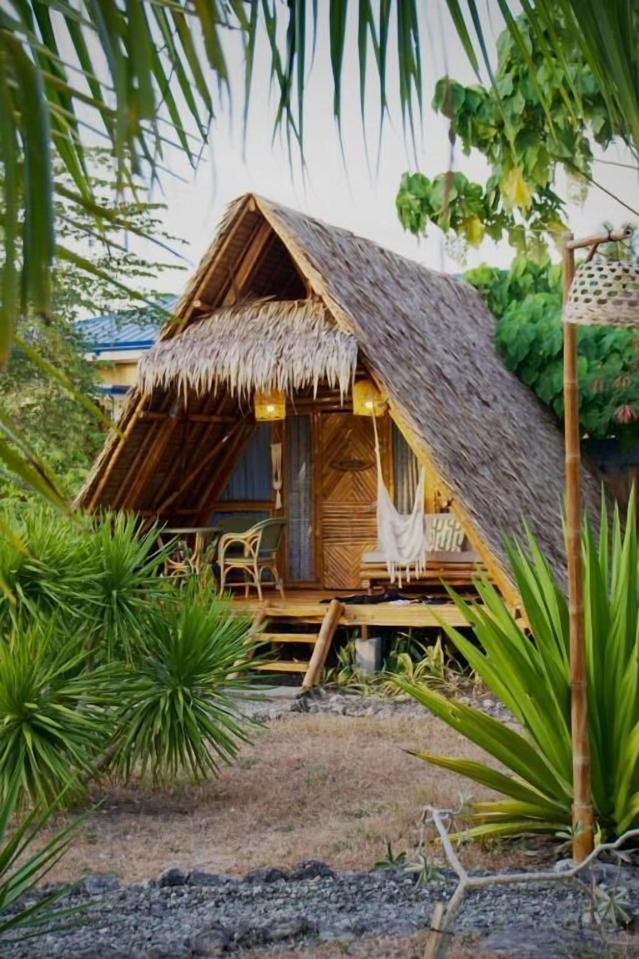 Una cabaña con techo de paja y una terraza de madera con zona de estar al aire libre.