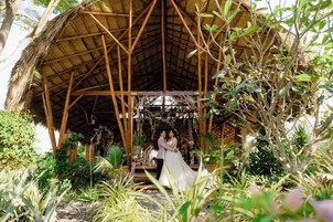 A couple embracing under a thatched structure surrounded by lush greenery.