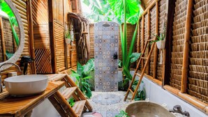 A bathroom with a large bathtub, a wooden vanity with a bowl sink, bamboo walls, and a tiled shower area. - Tongo Hill Cottages (Moalboal)