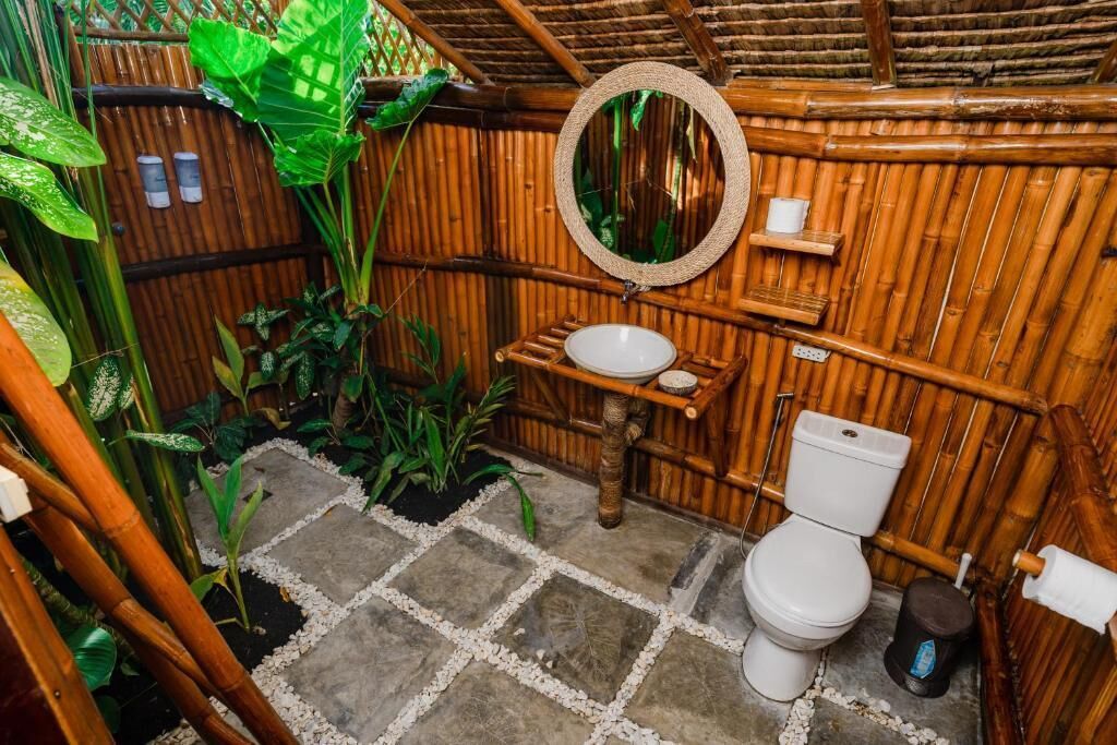 A bamboo-walled bathroom with a white toilet, a round mirror, and a small shelf.