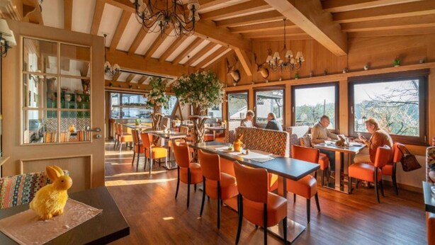 Ein Restaurant mit Holzbalken, orangefarbenen Stühlen und großen Fenstern.