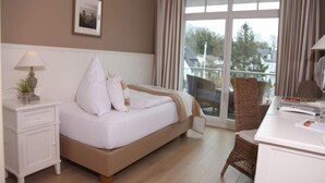 Habitación de hotel con cama, mesita de noche con lámpara, una silla y vistas al exterior.