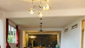 A living room with a sofa, a dining area with a table and chairs, a kitchen with a stone wall, and a chandelier. - sunrise high above the lake 1 (San Pedro La Laguna)