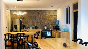 A modern kitchen with a stone wall, a dining area with a wooden table and chairs, and a hanging light fixture. - sunrise high above the lake 1 (San Pedro La Laguna)
