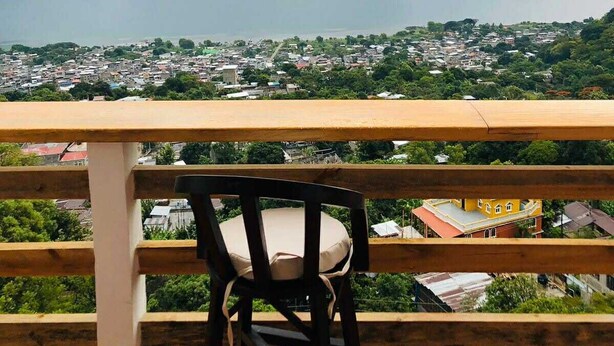 A chair on a balcony overlooking a cityscape with a large body of water and mountains in the distance. - sunrise high above the lake 1 (San Pedro La Laguna)