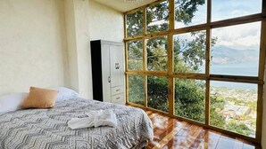 A bedroom with a large window, a bed, a wardrobe, and a chandelier. - sunrise high above the lake 1 (San Pedro La Laguna)