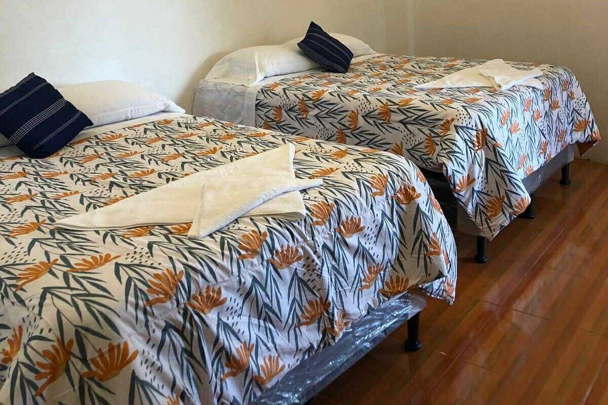 A room with two beds, each with patterned bedding, a hanging light fixture, and wooden flooring.