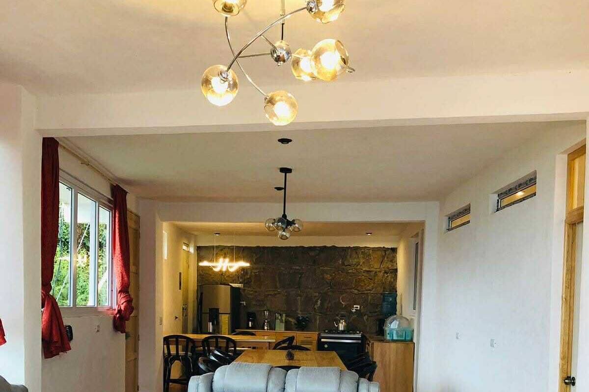 A living room with a sofa, a dining area with a table and chairs, a kitchen with a stone wall, and a chandelier.