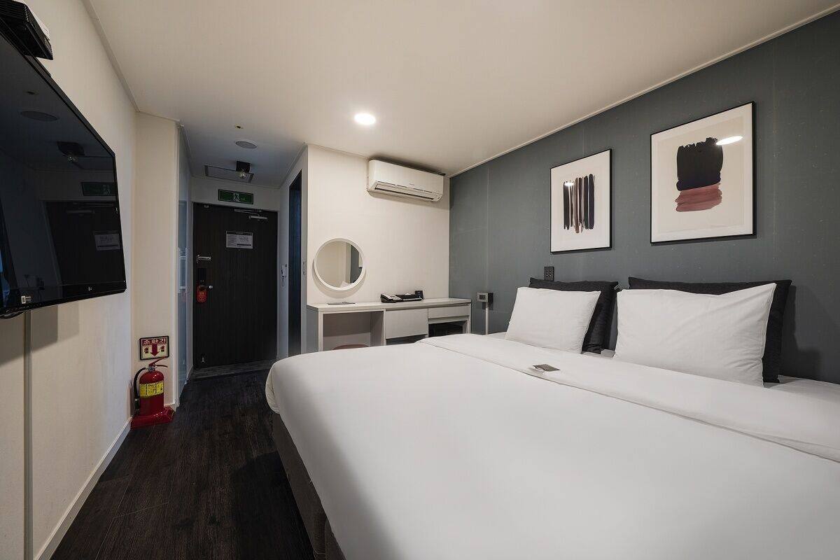 A hotel room with a bed, a desk, a mirror, and artwork on the wall.