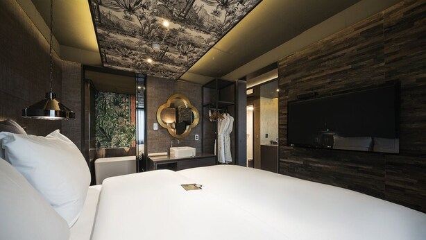 Une chambre d’hôtel moderne dotée d’un grand lit, d’un téléviseur fixé au mur, d’une coiffeuse avec un miroir et d’une fresque peinte au plafond.