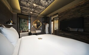 Una habitación de hotel moderna con una cama grande, un televisor montado, un tocador con espejo y un mural en el techo.