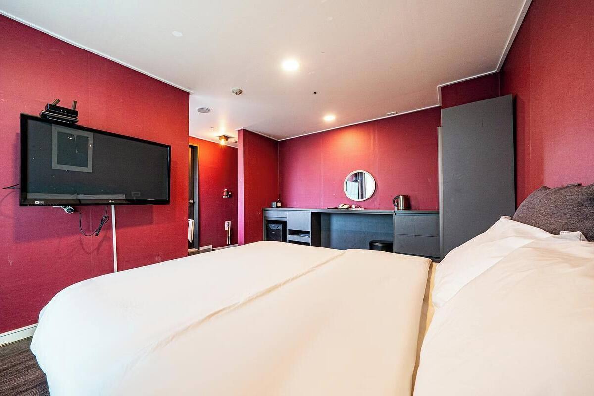 A hotel room with a large bed, a television mounted on the wall, a desk with a mirror, and a wardrobe.