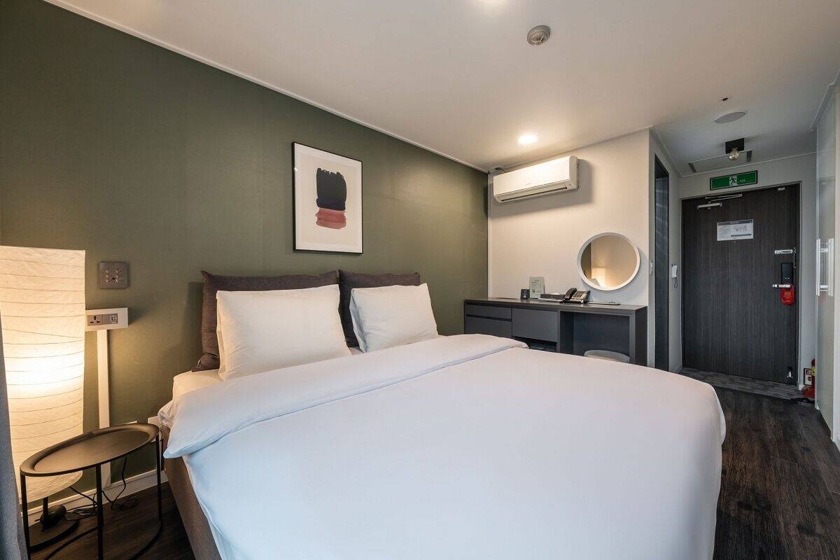 A hotel room with a bed, bedside table, lamp, and a mirror.
