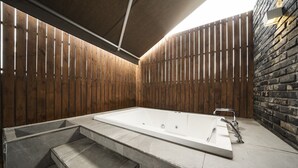 Un espace spa comprenant une grande baignoire, un petit coin salon et un mur en pierre.