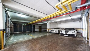 Un parking abritant deux voitures de sport blanches, avec des tuyaux apparents et un sol carrelé.