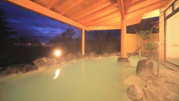 A hot spring area with wooden beams, rocks, and a glass door leading outside.