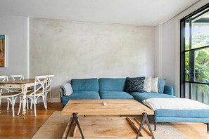 A modern living room with a blue sofa, a wooden coffee table, and a dining area with white chairs. - Sleek Tempe Pad near SYD Airport & Transit (Tempe)