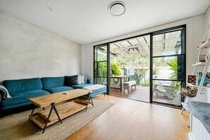 A modern living room with a teal sofa, a wooden coffee table, and a sliding glass door leading to an outdoor patio. - Sleek Tempe Pad near SYD Airport & Transit (Tempe)