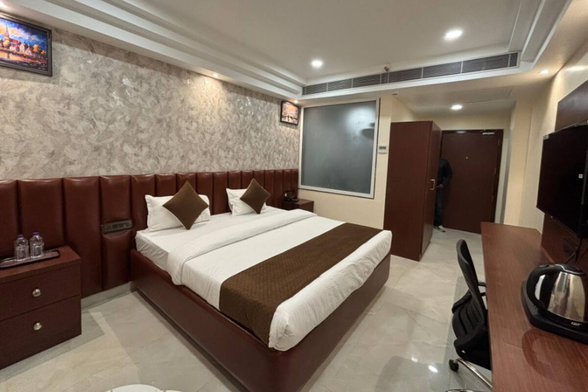 Quarto de hotel com cama, escrivaninha, cadeira, armário e televisão.