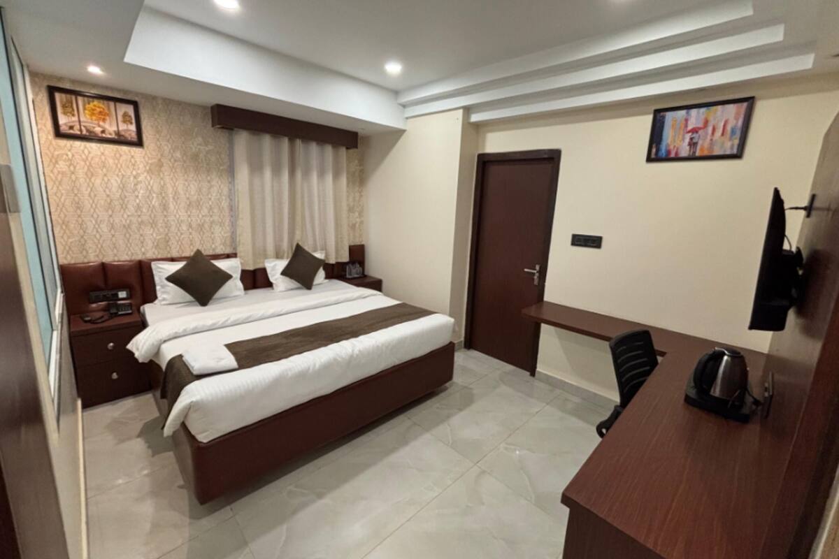 Quarto de hotel com cama, mesas de cabeceira, escrivaninha, cadeira, televisão e porta.