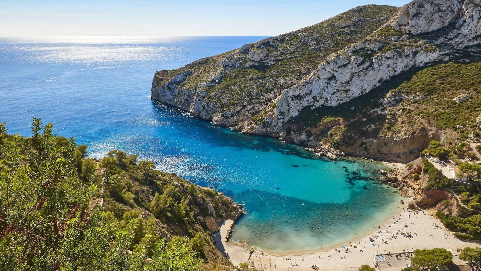 A coastal landscape with a beach, rocky cliffs, and clear blue waters.