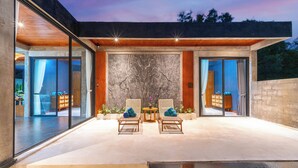A modern house with a patio, two wicker chairs, a small table, and a pool. - Melasti Beach Villa (Ungasan)