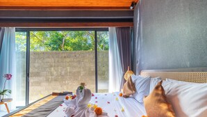 A hotel room with a bed, a view of greenery outside, and a window with curtains. - Melasti Beach Villa (Ungasan)