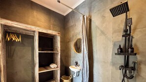 Un baño con tocador de madera, lavamanos, ducha y perchero para toallas.