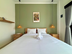 Ein ordentlich bezogenes Bett mit weißen Leinentüchern, zwei Nachttische, ein an der Wand hängendes Bild und zwei Pendelleuchten.