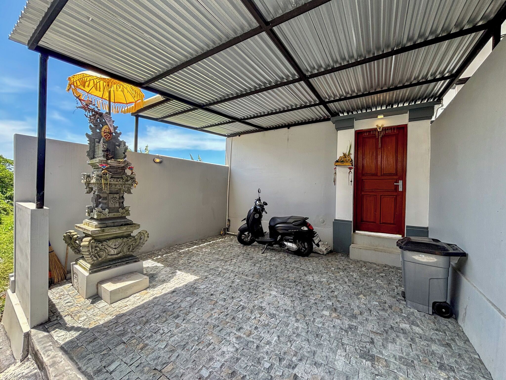 A covered outdoor area with a stone statue, a red door, and a parked scooter.