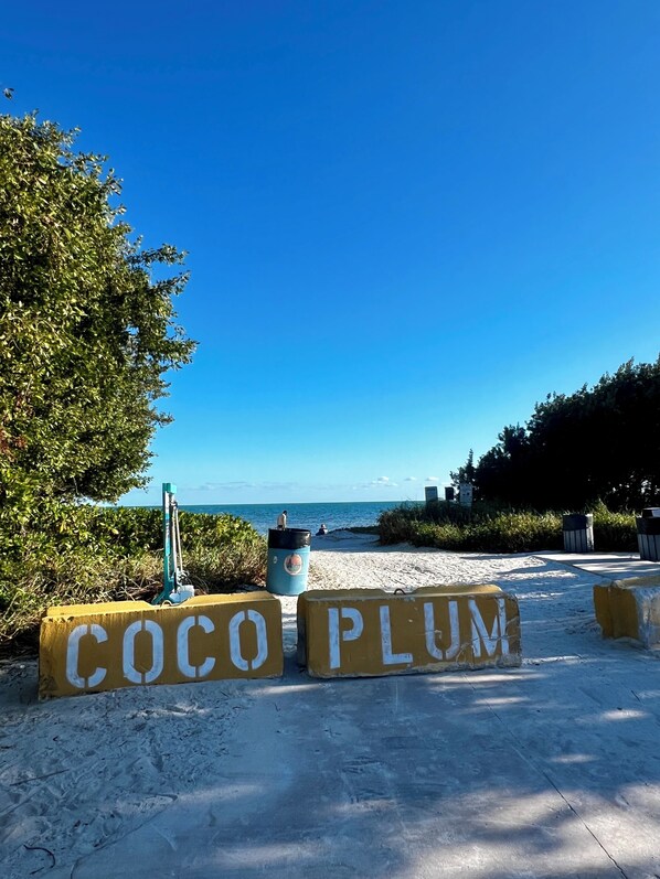 A beach entrance with 'COCO PLUM' signboards and a clear view of the ocean.