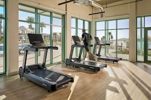 A gym with treadmills, large windows, and a view of a pool and palm trees.