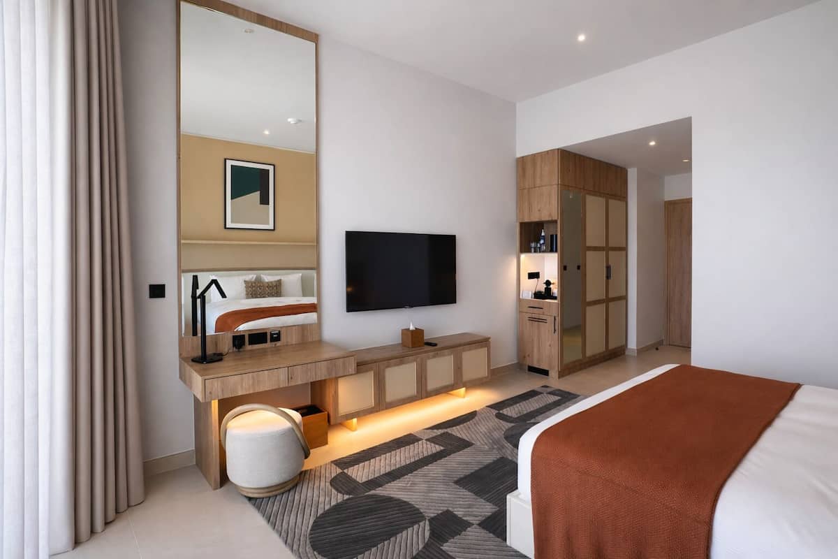 Una habitación de hotel moderna con una cama grande, un televisor montado en la pared, un escritorio de madera con una silla y un armario.
